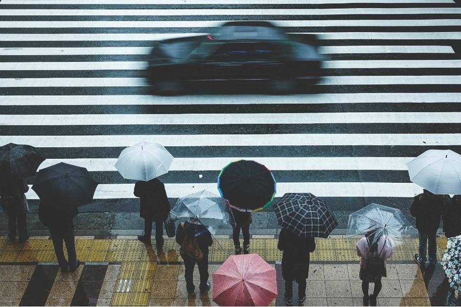 tiotal personer med paraply väntar vid ett övergångsställe på en förbipasserande bil.jpg