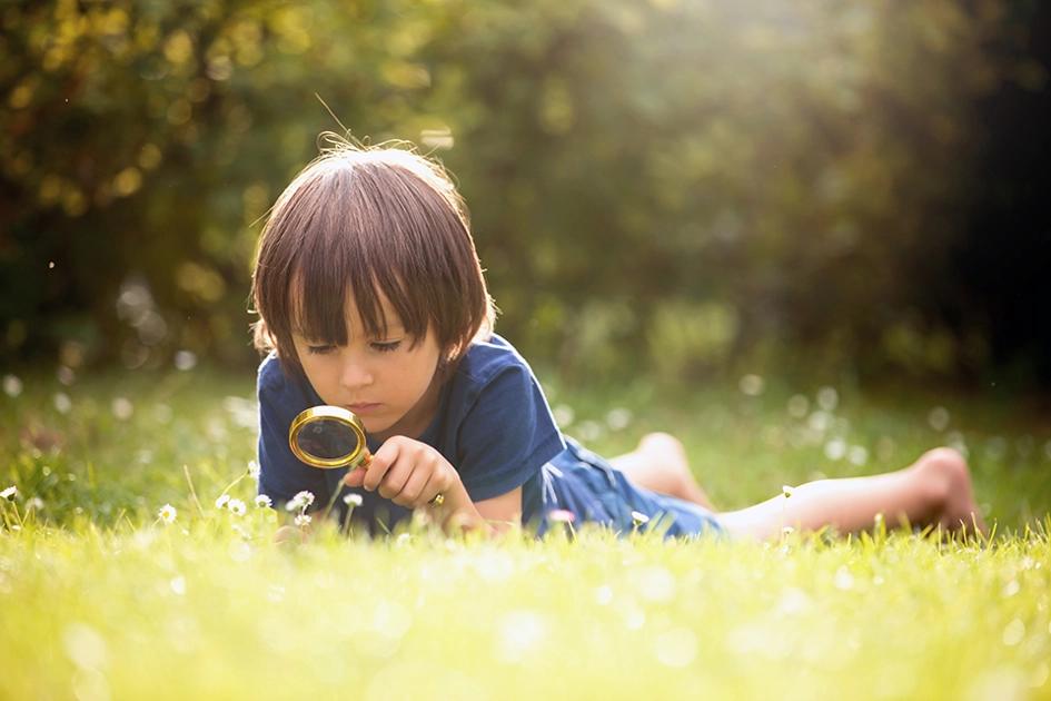 pojke ligger och tittar ner i gräset med förstoringsglas.jpg