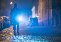 man går på kullerstensgata i natten och lyser med ficklampa mot kameran.jpg