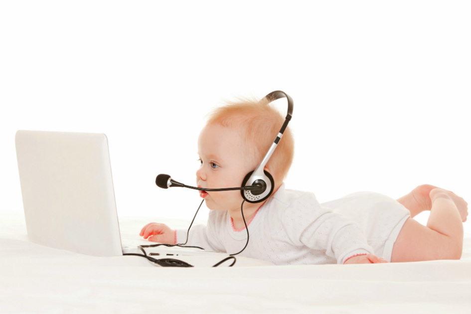bebis ligger på mage med headset och tittar in i skärmen på en laptop.jpg