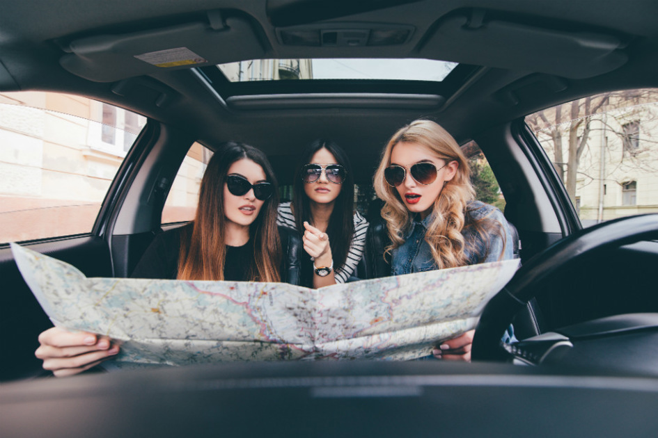 tre tjejer i en bil tittar på en stor karta.jpg