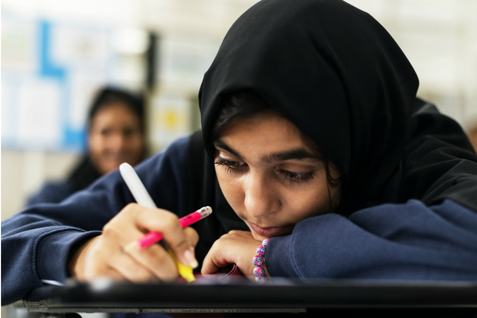 tjej från mellanöstern sitter med huvudet nära sin skolbänk och skriver.jpg