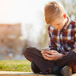 kille sitter utomhus och tittar i sin mobiltelefon.jpg