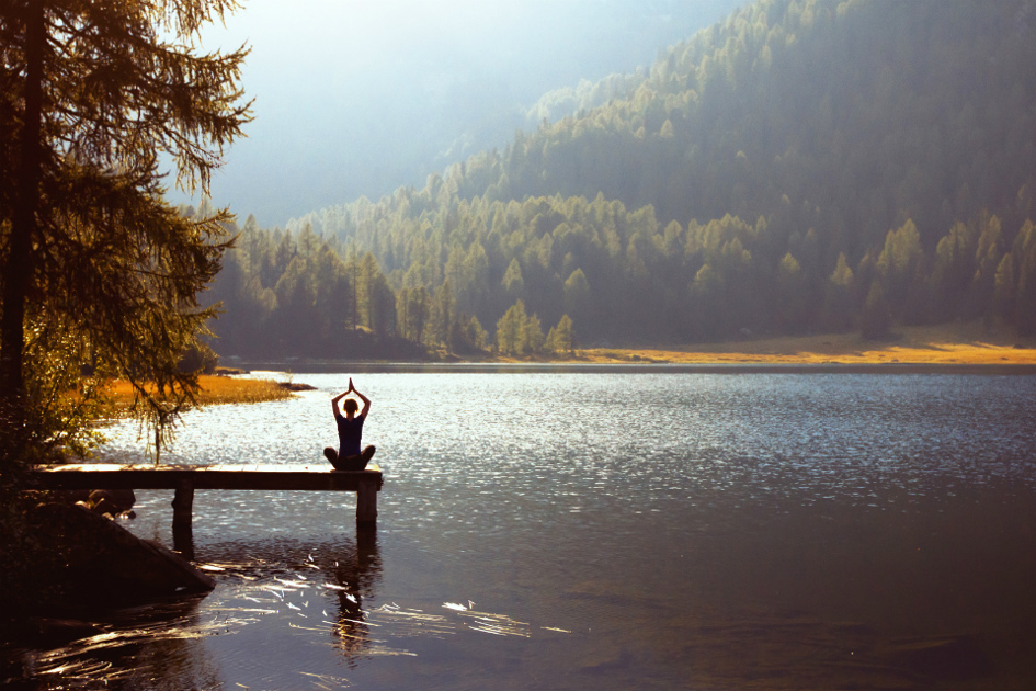 människa sitter på en brygga och mediterar i ett skogslandskap.jpg