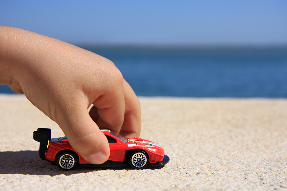 ett barns hand drar en leksaksbil på stranden.jpg