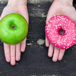 två händer håller fram ett äpple i ena handen och en donut i andra.jpg
