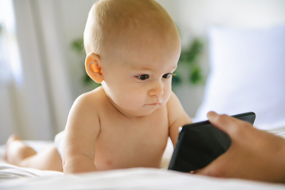 spädbarn tittar i mobil som en vuxen håller i.jpg