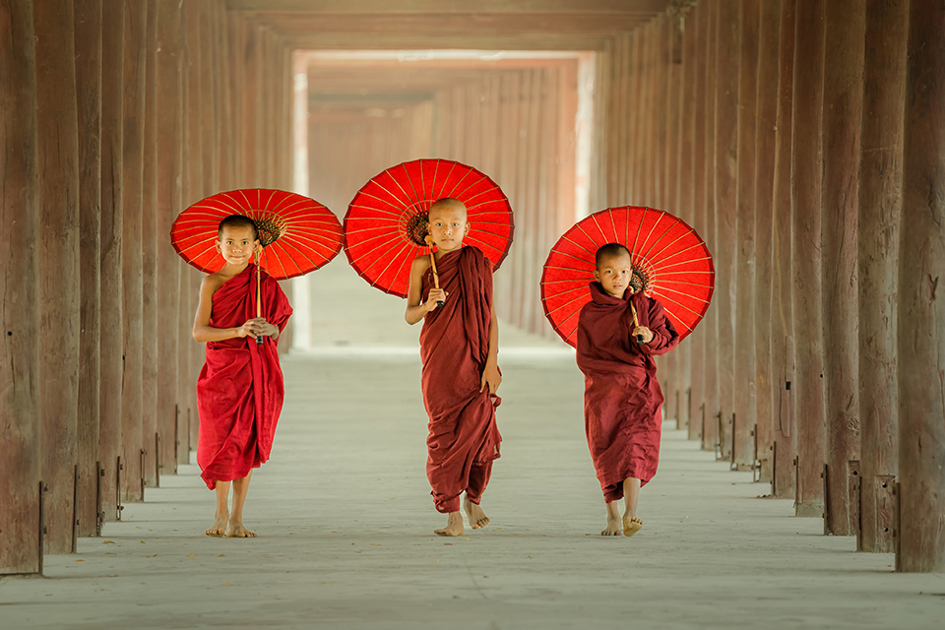 tre unga munkpojkar i tibet går med varsitt paraply i tempel.jpg