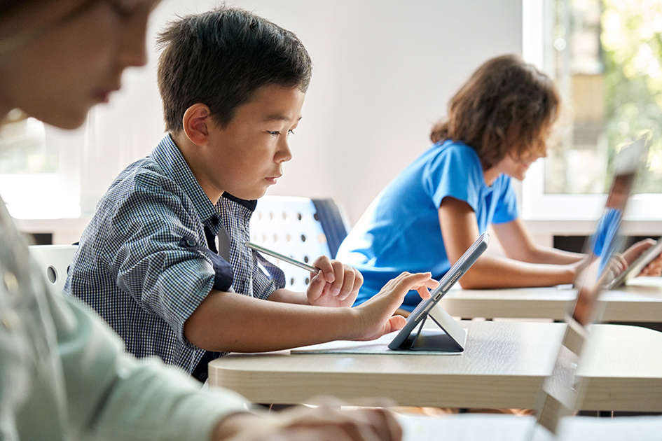 It I Skolan, Digitalisering, Kille Sitter Vid Skolbänken Och Arbetar I Lärplatta